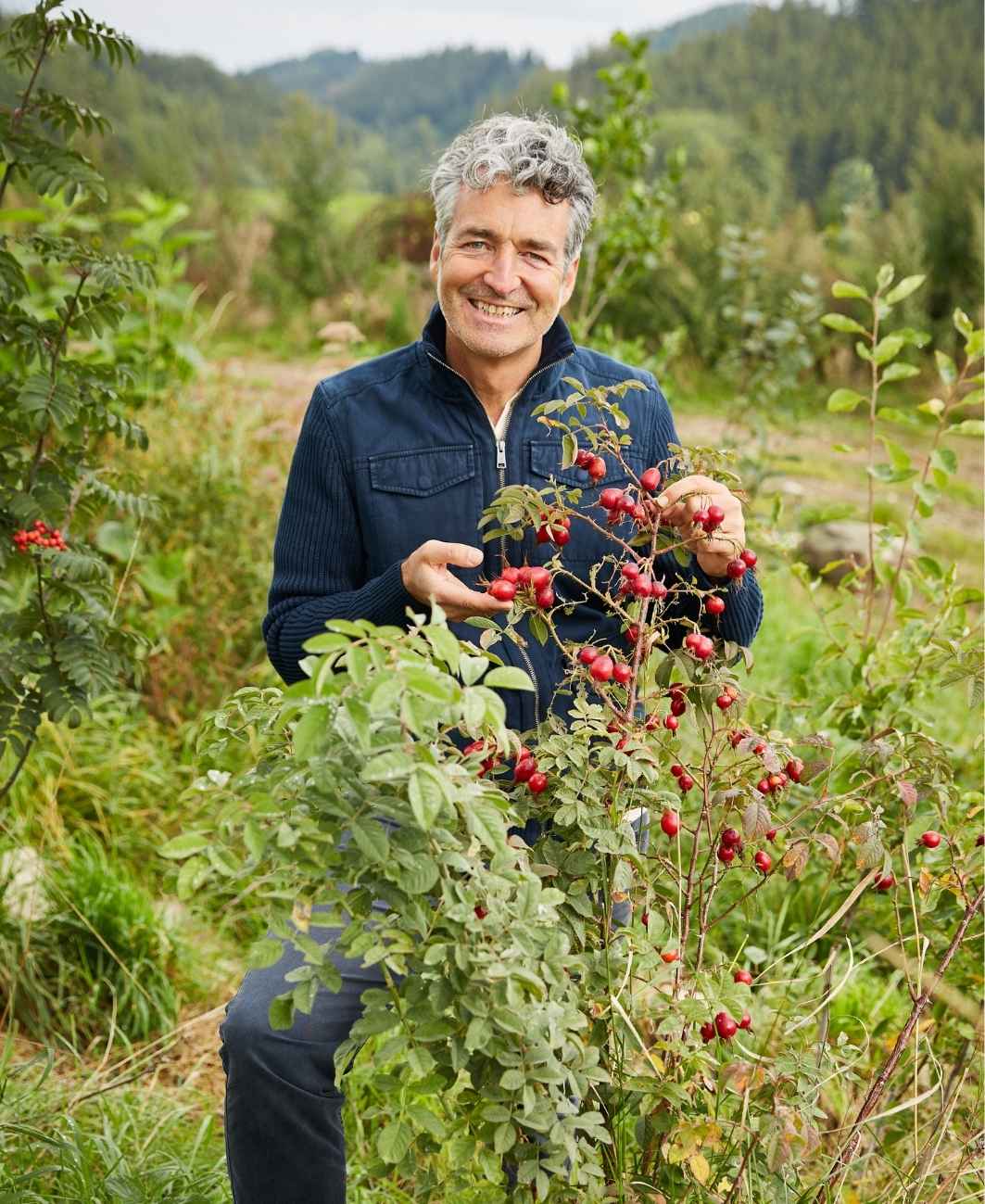 Markus Strauß steht lächelnd an einem Strauch voller roter Früchte in freier Landschaft