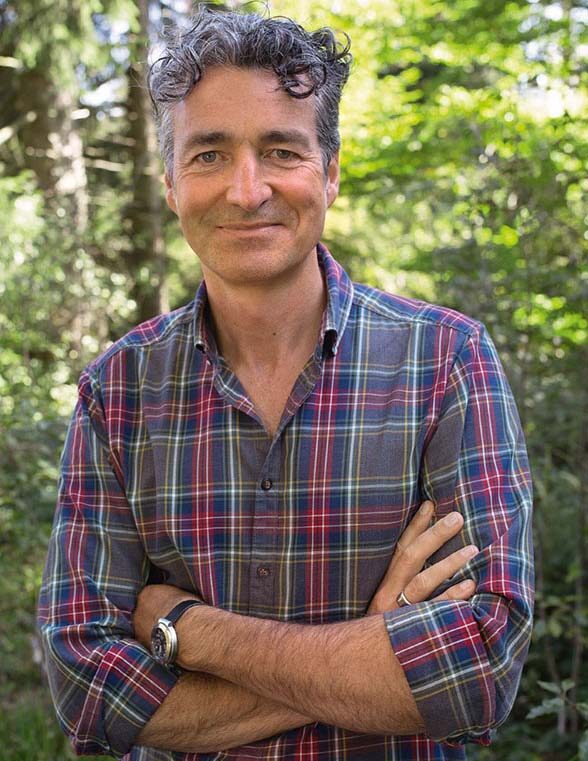 Markus Strauß im Karohemd mit verschränkten Armen vor sonnigem Wald