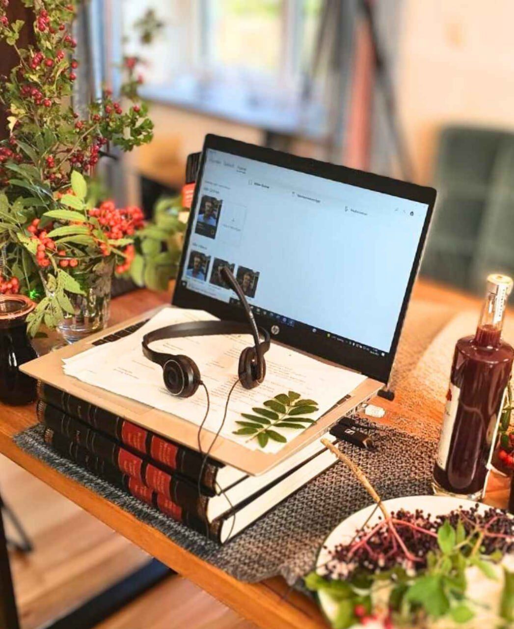 Laptop mit laufender Videokonferenz auf einem Tisch, davor Headset, Unterlagen, Bücher und Wildfrüchte